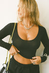 Front view of model posing in the fitted soft black modal Scoop Neck Long Sleeve top with a deep scoop neckline and fitted sleeves