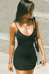 Front view of model posing in the form fitting stretchy black rib mini Slip Dress with thin straps, a u neckline and a tiny side slit at the hem