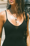 Close up detail front view of model posing in the form fitting stretchy black rib mini Slip Dress with thin straps, a u neckline and a tiny side slit at the hem