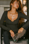 Front view of model sitting in a chair and posing in the fitted vintage black Henley Long Sleeve with a notch in the scoop neckline