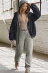 Full body front view of model posing in the form fitting taupe flexrib Invisible Zip Long Sleeve top with a 3/4 front invisible zipper and a crew neckline