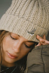 Close up detail front view of model posing in the soft and warm oat Knit Beanie that has removable custom JOAH BROWN pin.