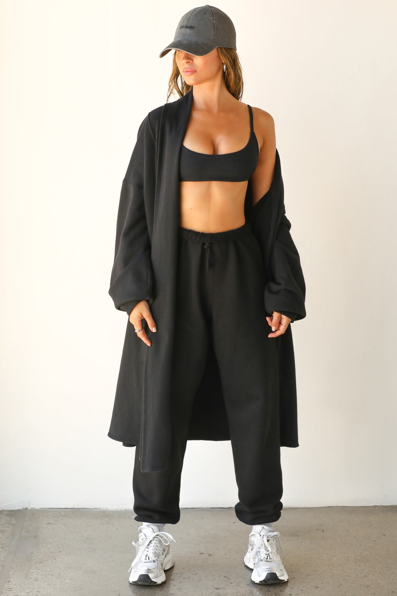 Full body front view of model posing in the knee-length loose fitting black french terry Oversized Cardigan with a rolled neckline and extra long sleeves