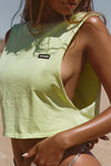 Close up side view of model posing in the relaxed fit melon cotton Cut Off Boyfriend Tank with low cut armholes, a crew neckline and a joah brown logo patch at the upper left chest