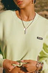 Close up front view of model posing in the loose fit cropped melon french terry Cut Off Sweatshirt with oversized long sleeves, a raw cut hem and a white patch with a black joah brown logo on it sewn on the upper left chest