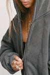 Close up detail front view of model zipping up the oversized comfortable washed black french terry Oversized Zip Hoodie with a full length front zip closure, side pockets and thumbholes in the fitted cuffs