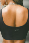 Close up detail back view of model posing in the fitted sueded onyx Scoop Neck Smoothing Bra top with a scoop back and Joah Brown logo patch that can be worn in the front or the back