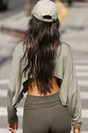 Back view of model posing in the street wearing the cropped, loose fitting sage modal Relaxed Crop Long Sleeve top with a wide scoop neckline that can be worn off the shoulder