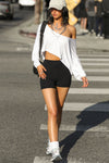 Full body front view of model posing in the street wearing the cropped, loose fitting white modal Relaxed Crop Long Sleeve top with a wide scoop neckline that can be worn off the shoulder