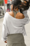 Back view of model posing outside in the street wearing the oversized pearl grey french terry Slouchy Pullover Sweatshirt with a wide, off-the-shoulder neckline and a JOAH BROWN logo patch on the right sleeve