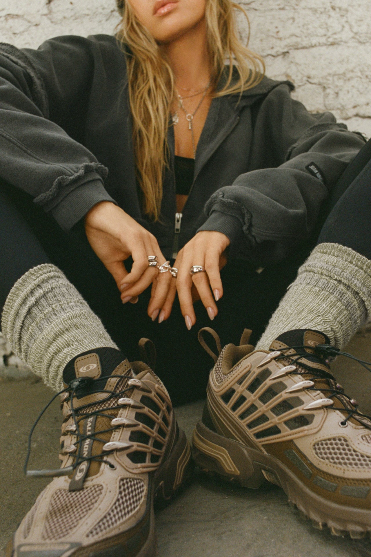 Front view of model sitting on the floor posing in the crew-style ribbed and soft heathered olive Merino Stripe Sock