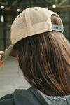 Back view of model posing the trucker style green/khaki Mesh Back Cap with a curved brim and stitched eyelets. Features a mesh back, snap-back closure and an embroidered Joah Brown logo on the front.