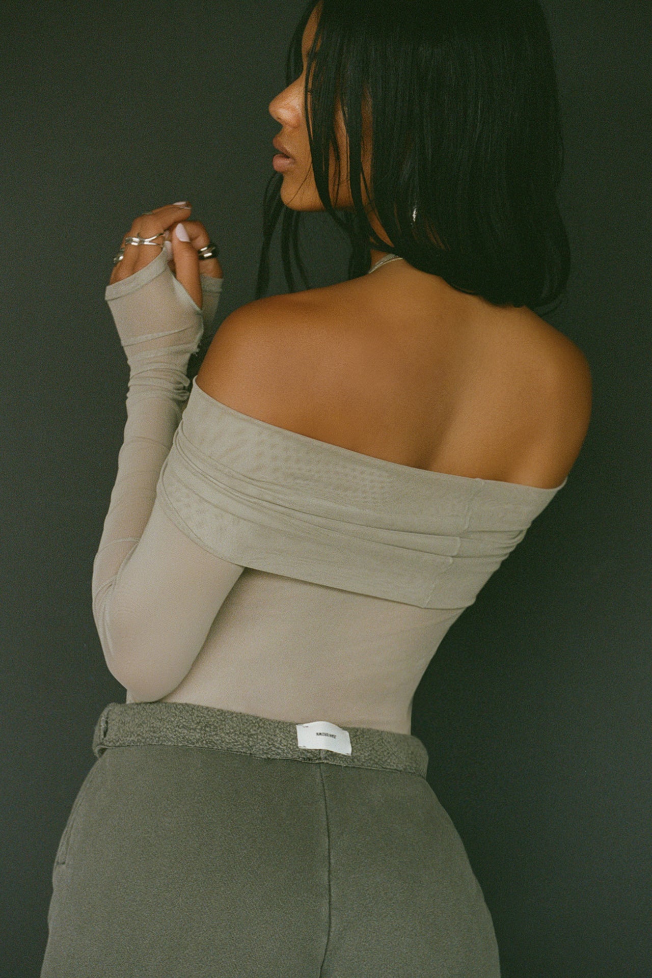 Back view of model posing in the fitted dew mesh Off The Shoulder Long Sleeve top with a folded off-the-shoulder neckline and thumbholes in the sleeves