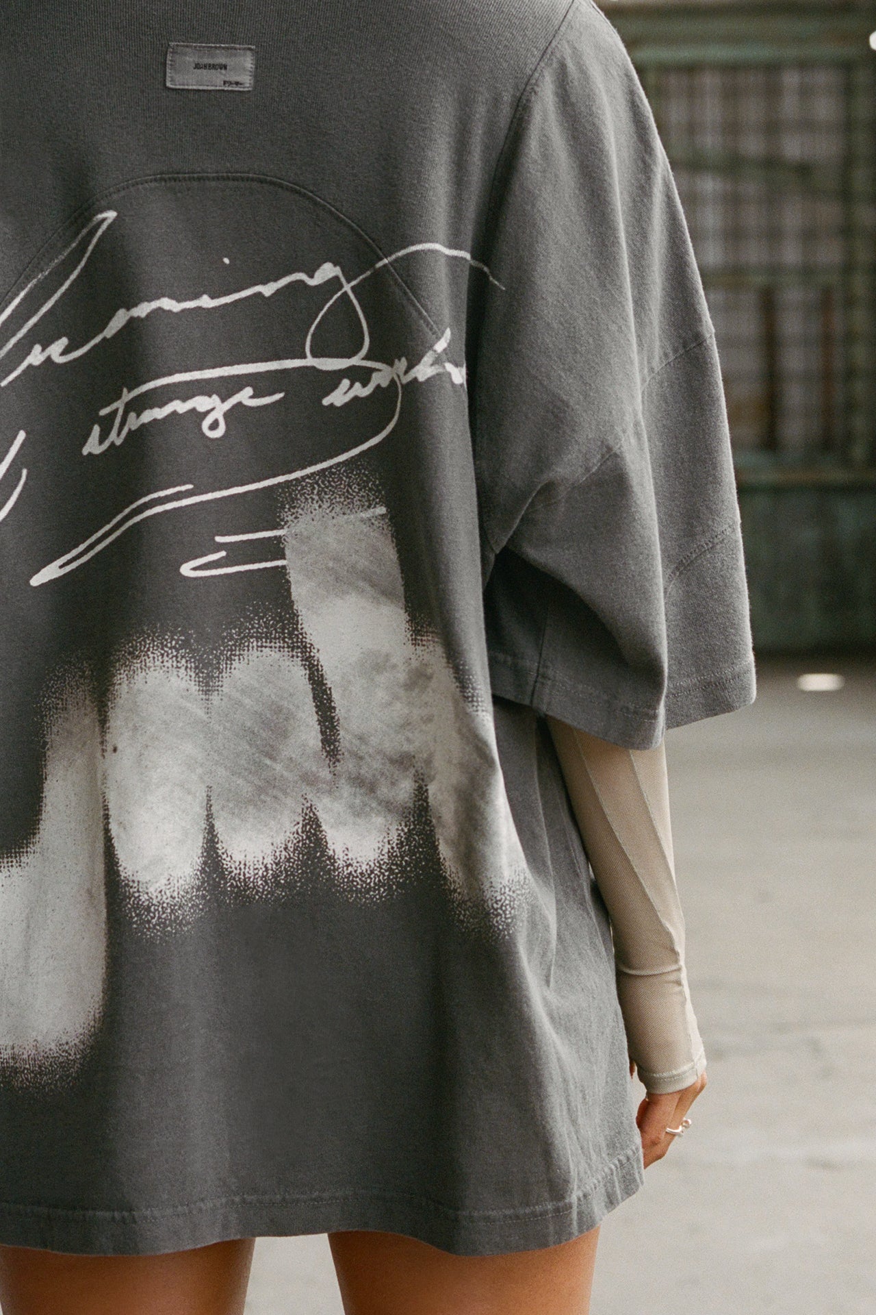 Close up back view of model posing in the oversized washed black cotton Original Graphic Tee with panel details and custom screen print graphic “dreaming of a strange world” on the back