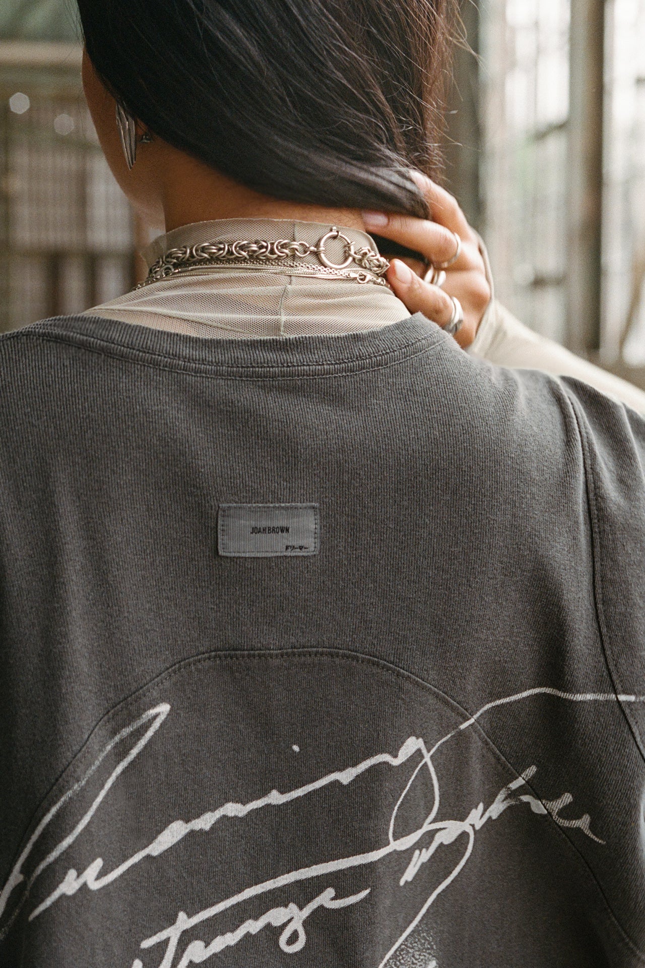 Close up back view of model posing in the oversized washed black cotton Original Graphic Tee with panel details and custom screen print graphic “dreaming of a strange world” on the back