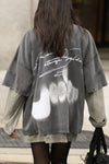 Back view of model walking in the street and posing in the oversized washed black cotton Original Graphic Tee with panel details and custom screen print graphic “dreaming of a strange world” on the back