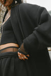 Closeup view of model posing in the knee-length loose fitting black french terry Oversized Cardigan with a rolled neckline and extra long sleeves