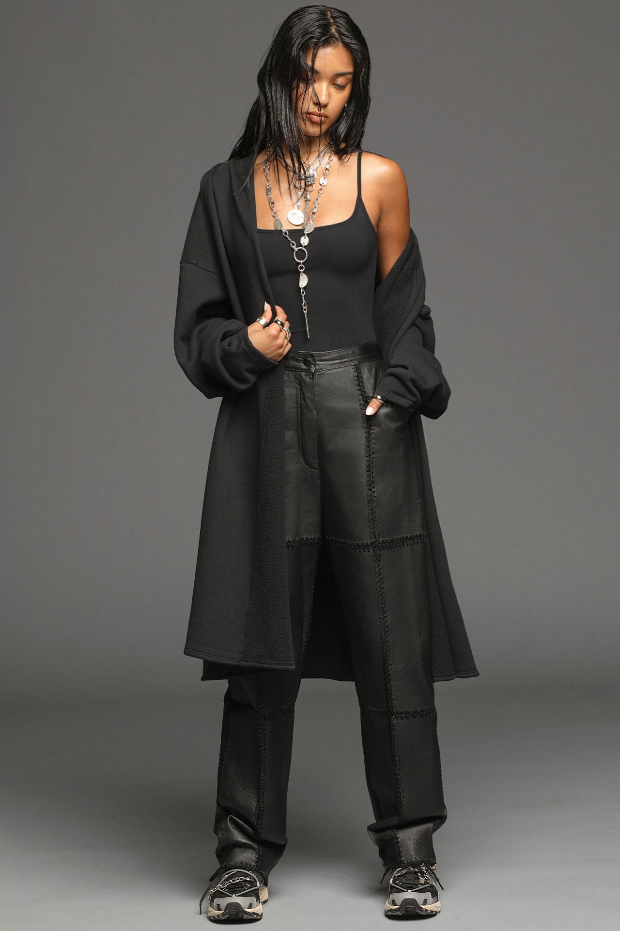 Full body front view of model posing in the knee-length loose fitting black french terry Oversized Cardigan with a rolled neckline and extra long sleeves