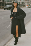 Full body front view of model posing in the knee-length loose fitting black french terry Oversized Cardigan with a rolled neckline and extra long sleeves