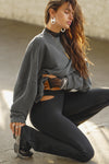 Side view of model kneeling on the floor and posing in the relaxed fit washed black french terry Oversized Crew Pullover sweatshirt with dropped sleeves and a ribbed crew neckline