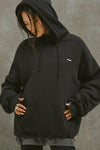 Front view of model posing in the oversized comfortable black french terry Oversized Pullover Hoodie sweatshirt with a Joah Brown logo patch at the front left chest, kangaroo pocket, drawstrings and thumbholes