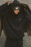 Front view of model posing in the oversized comfortable black french terry Oversized Pullover Hoodie sweatshirt with a Joah Brown logo patch at the front left chest, kangaroo pocket, drawstrings and thumbholes