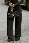 Front view of model from the waist down posing in the relaxed fit black french terry Oversized Straight Leg Jogger with an elastic waistband, hidden drawstring, pocket details. and adjustable cinching at the ankle cuffs