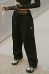 Front view of model from the waist down posing in the relaxed fit black french terry Oversized Straight Leg Jogger with an elastic waistband, hidden drawstring, pocket details. and adjustable cinching at the ankle cuffs