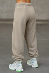 Back view of model from the waist down posing in the relaxed fit sand french terry Oversized Straight Leg Jogger with an elastic waistband, hidden drawstring, pocket details. and adjustable cinching at the ankle cuffs