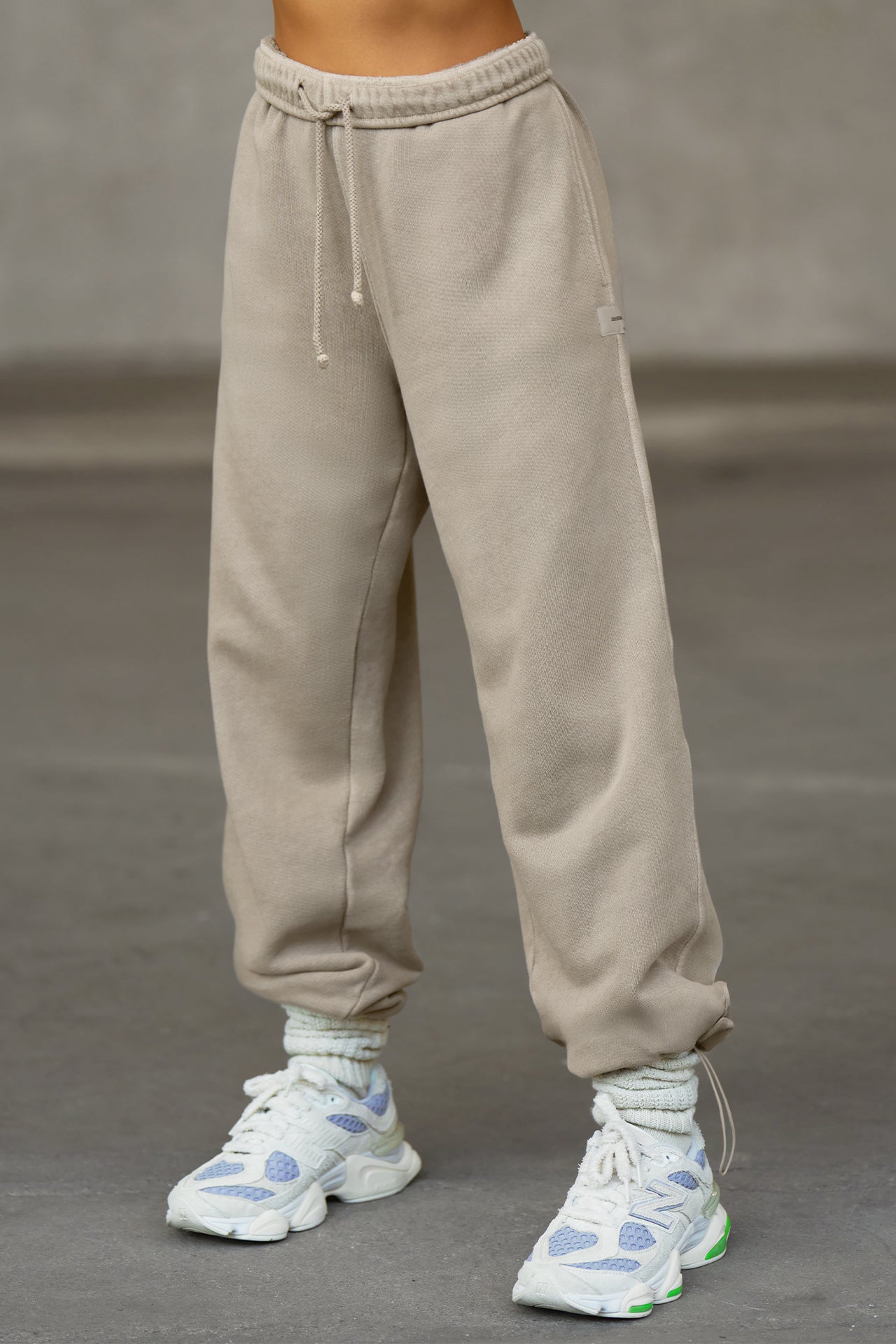 Front view of model from the waist down posing in the relaxed fit sand french terry Oversized Straight Leg Jogger with an elastic waistband, hidden drawstring, pocket details. and adjustable cinching at the ankle cuffs