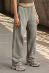 Front  view of model from the waist down posing in the relaxed fit vetiver french terry Oversized Straight Leg Jogger with an elastic waistband, hidden drawstring, pocket details. and adjustable cinching at the ankle cuffs