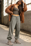 Full body front of model posing in the relaxed fit vetiver french terry Oversized Straight Leg Jogger with an elastic waistband, hidden drawstring, pocket details. and adjustable cinching at the ankle cuffs