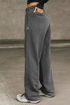 Side view of model from the waist down posing in the relaxed fit washed black french terry Oversized Straight Leg Jogger with an elastic waistband, hidden drawstring, pocket details. and adjustable cinching at the ankle cuffs