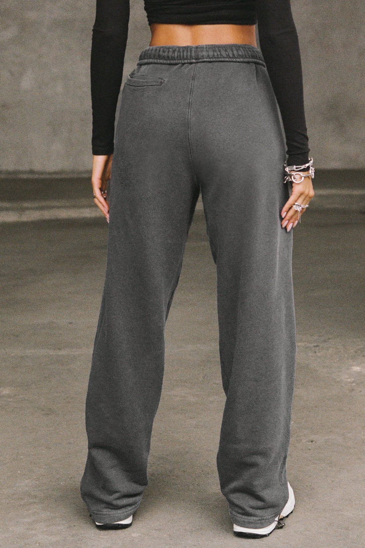 Back view of model from the waist down posing in the relaxed fit washed black french terry Oversized Straight Leg Jogger with an elastic waistband, hidden drawstring, pocket details. and adjustable cinching at the ankle cuffs