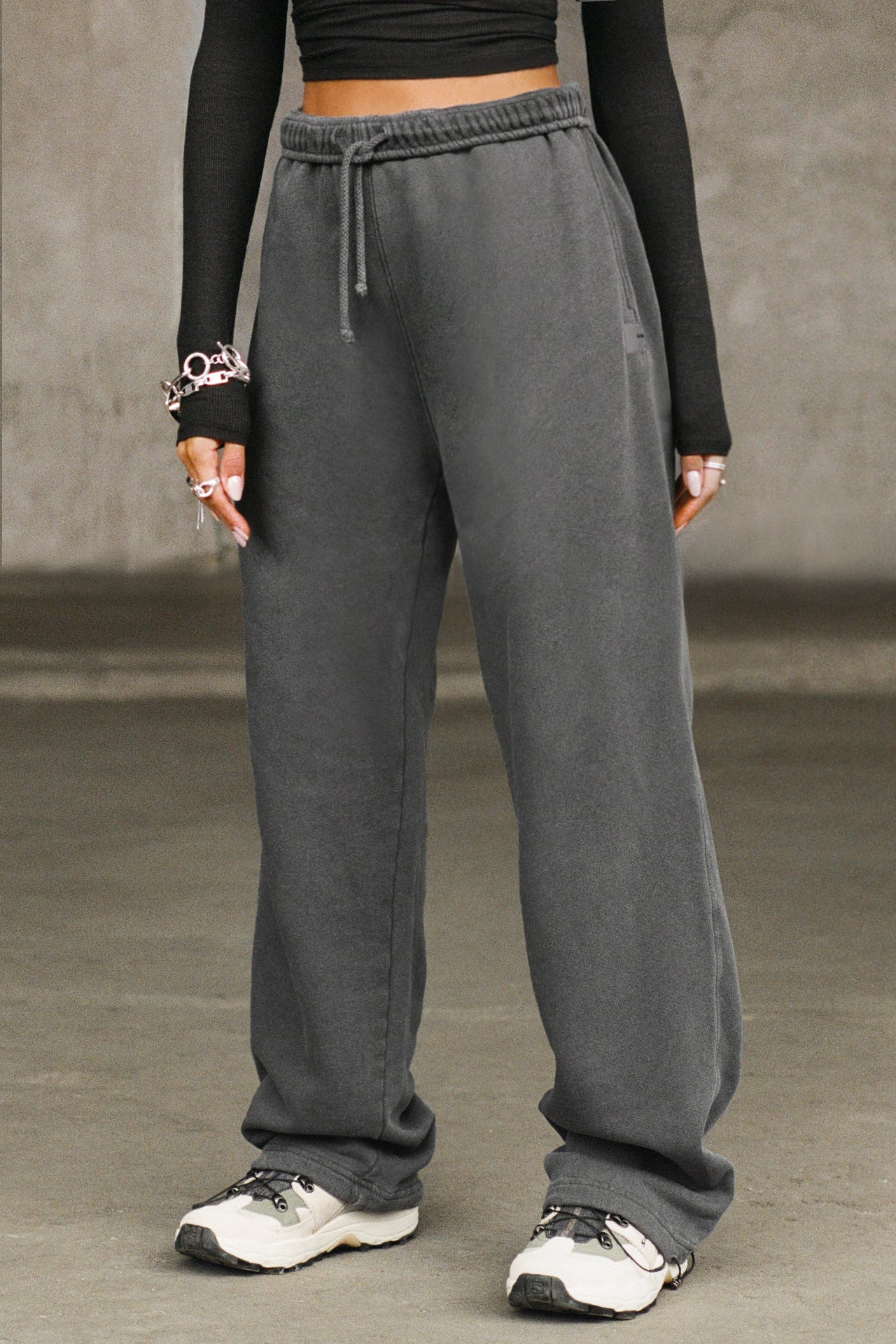 Front view of model from the waist down posing in the relaxed fit washed black french terry Oversized Straight Leg Jogger with an elastic waistband, hidden drawstring, pocket details. and adjustable cinching at the ankle cuffs