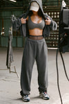 Full body front of model posing in the relaxed fit washed black french terry Oversized Straight Leg Jogger with an elastic waistband, hidden drawstring, pocket details. and adjustable cinching at the ankle cuffs