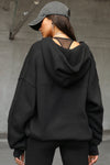 Back view of model posing in the oversized comfortable black french terry Oversized Zip Hoodie with a full length front zip closure, side pockets and thumbholes in the fitted cuffs