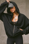 Front view of model posing in the oversized comfortable black french terry Oversized Zip Hoodie with a full length front zip closure, side pockets and thumbholes in the fitted cuffs