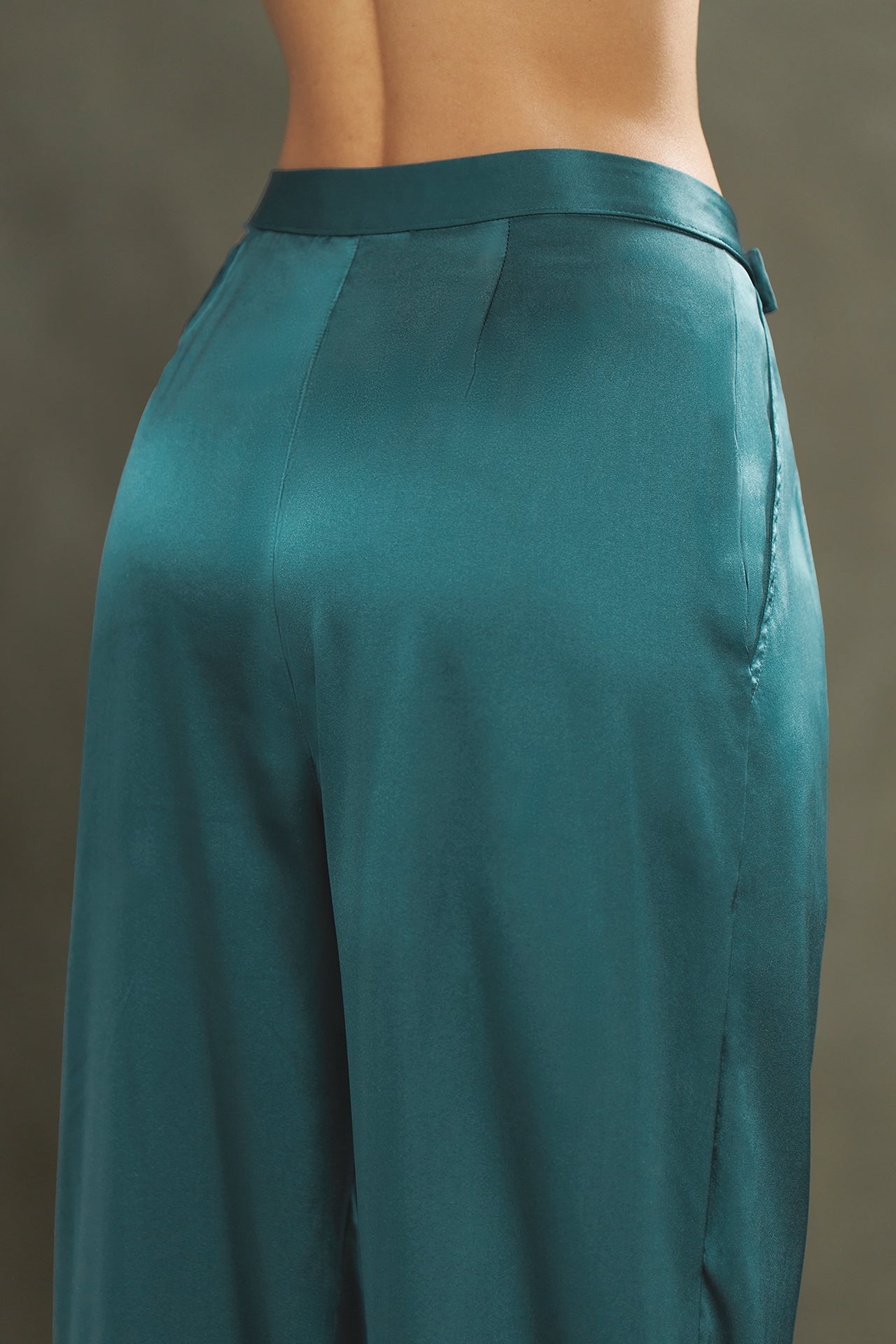 Close up detail back view of model from the waist down posing in the soft and smooth classic pleated lagoon silk Relaxed Silk Trouser with a flattering wide leg, zip fly and side pockets.