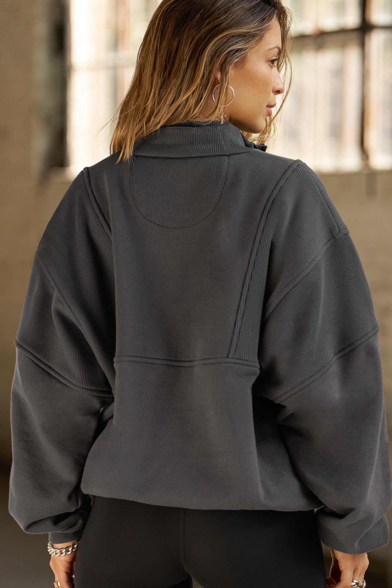 Back view of model posing in the oversized comfortable charcoal luxe french terry Retro Half Zip pullover sweatshirt with ribbed panels and accents on the back and sleeves and a high collar