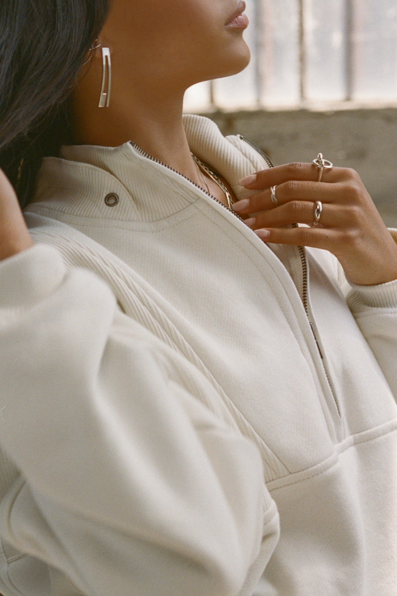 Close up detail side view of model posing in the oversized comfortable off white luxe french terry Retro Half Zip pullover sweatshirt with ribbed accents on the chest and sleeves, a hidden kangaroo pocket and a half zip collar