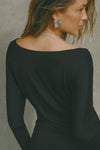 Back view of model posing in soft and lightweight black modal Ruched Asymmetrical Long Sleeve top with fitted sleeves, a relaxed asymmetrical hemline and a flattering ruched side detail.