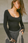 Front view of model posing in the fitted black flexrib Scoop Corset Long Sleeve with a scoop neckline, adjustable ties at the neck, and thumbholes in the mesh sleeves