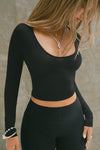 Front view of model posing the fitted lightweight black modal Scoop Neck Long Sleeve top with a deep scoop neckline and fitted sleeves