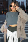 Front view of model posing in the street wearing the cropped relaxed fit evergreen cotton slouchy crop long sleeve top with a crew neckline, dropped shoulders and oversized sleeves