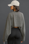 Back view of model posing in the cropped relaxed fit haze cotton Slouchy Crop Lonng Sleeve top with a crew neckline, dropped shoulders and oversized sleeves