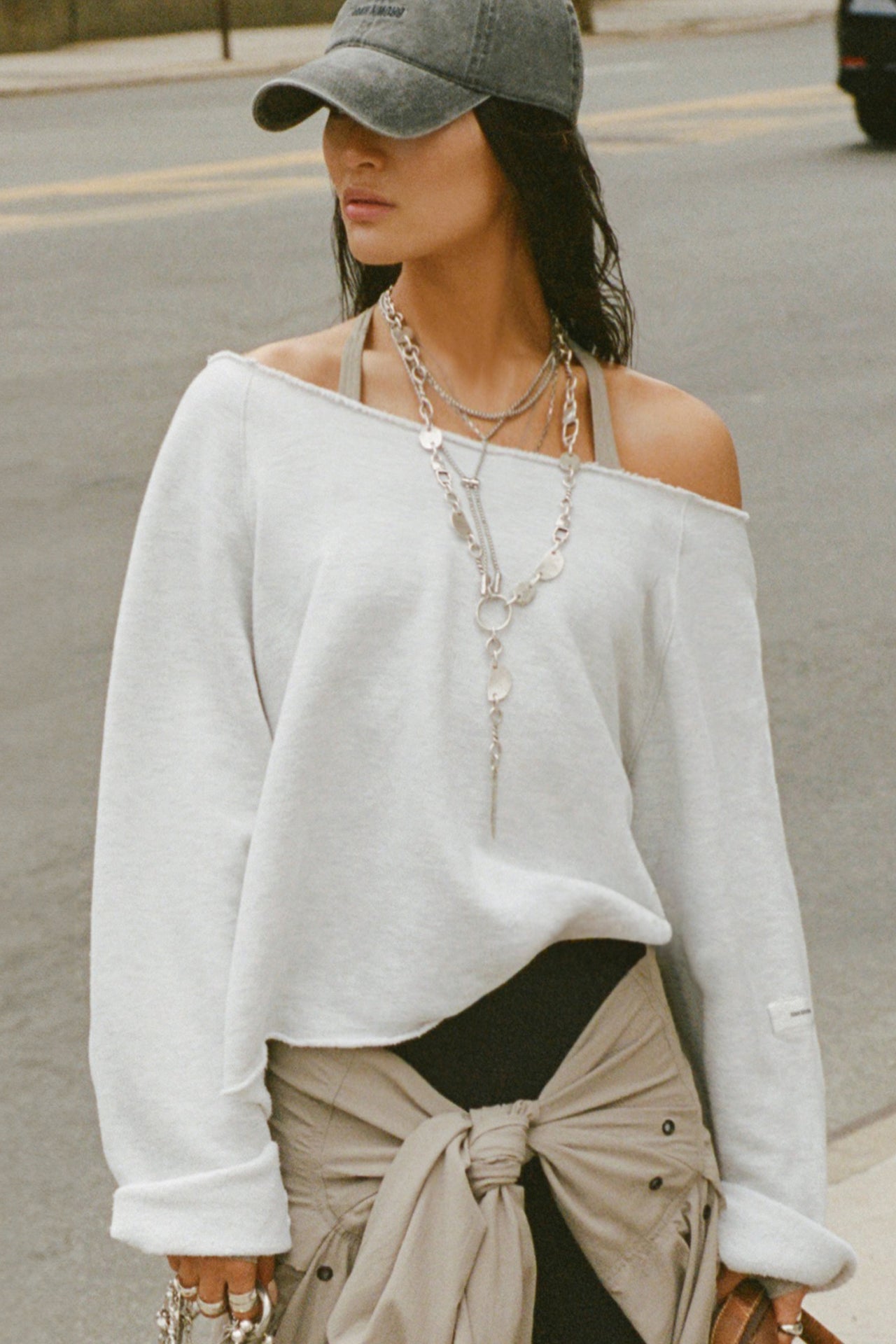 Front view of model posing outside in the street wearing the oversized pearl grey french terry Slouchy Pullover Sweatshirt with a wide, off-the-shoulder neckline and a JOAH BROWN logo patch on the right sleeve