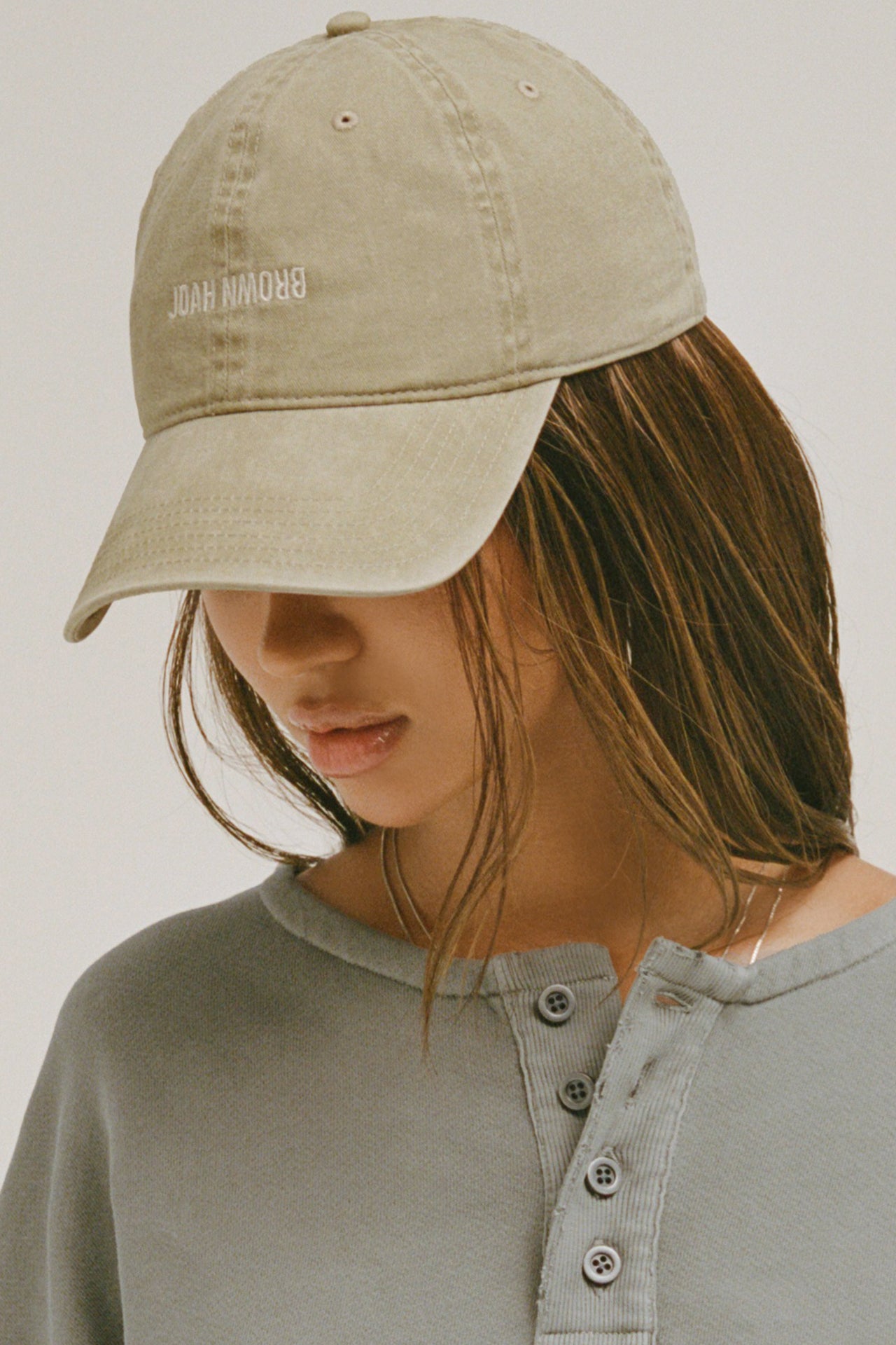 Side view of model wearing the six-panel desert Official Cap with a curved brim and an embroidered upside down Joah Brown logo on the front