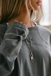 Close up detail front view of model posing in the oversized washed black cotton Vintage Panel Long Sleeve with a crew neckline, intricate panel details and eyelest on the chest and sleeve which you can thread jewelry through