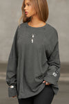 Front view of model posing in the oversized washed black cotton Vintage Panel Long Sleeve with a crew neckline, intricate panel details and eyelest on the chest and sleeve which you can thread jewelry through